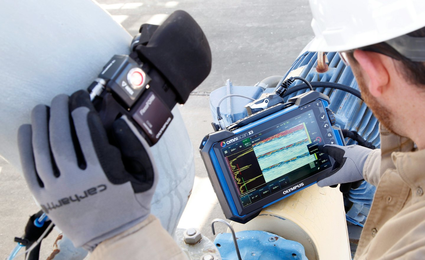 Un tecnico usa un sensore e un tablet per ispezionare un tubo industriale.